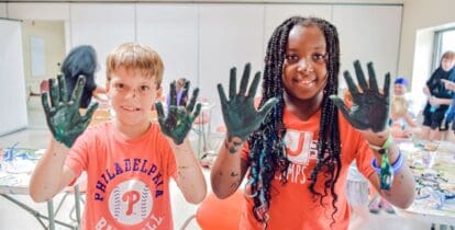 Two kids, one girl and one boy, showing off their messy hands after working on a science project.