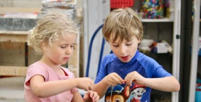 A girl and boy inside an arts and crafts room, putting together a bracelet.