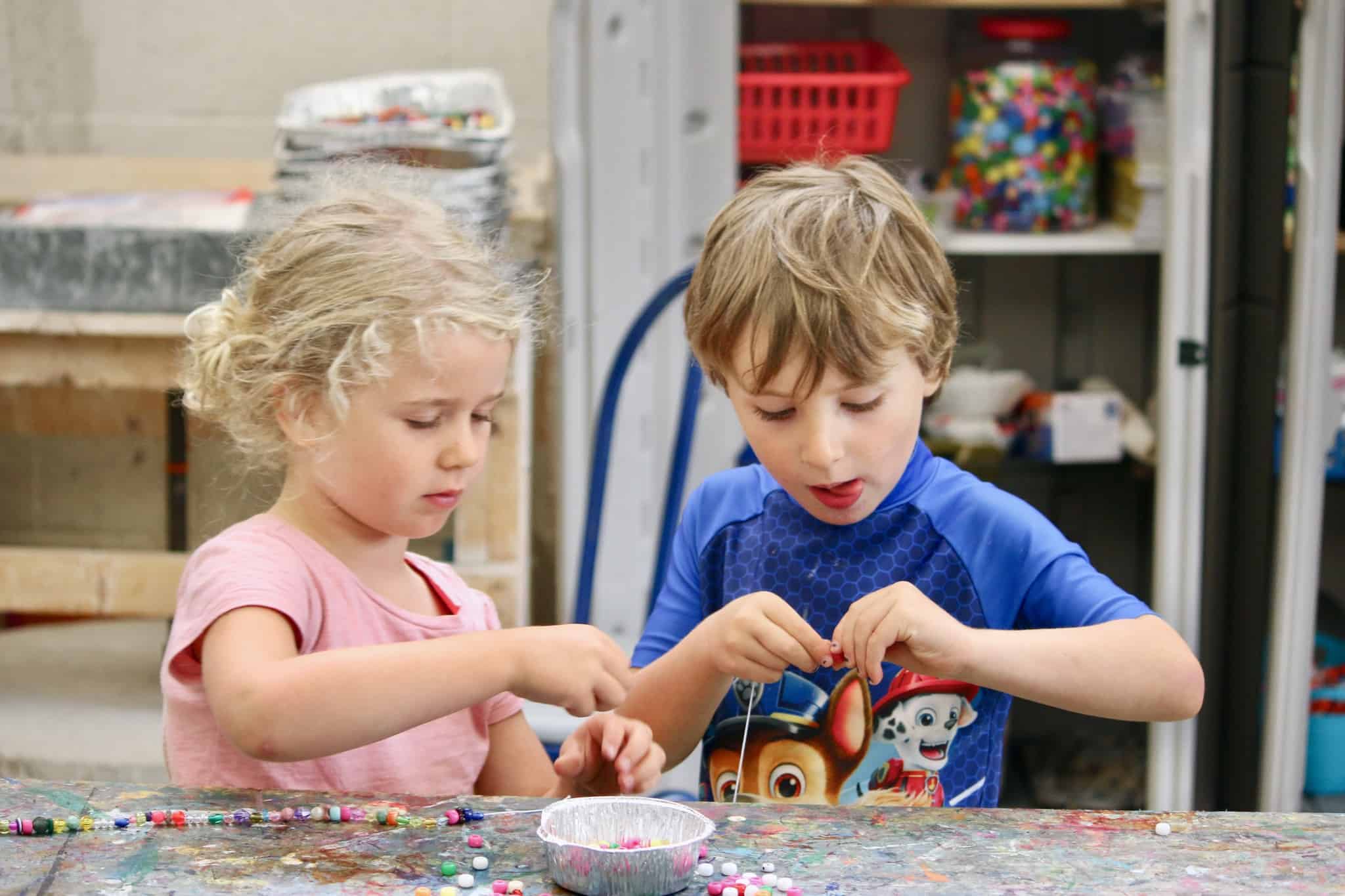 A girl and boy inside an arts and crafts room, putting together a bracelet.